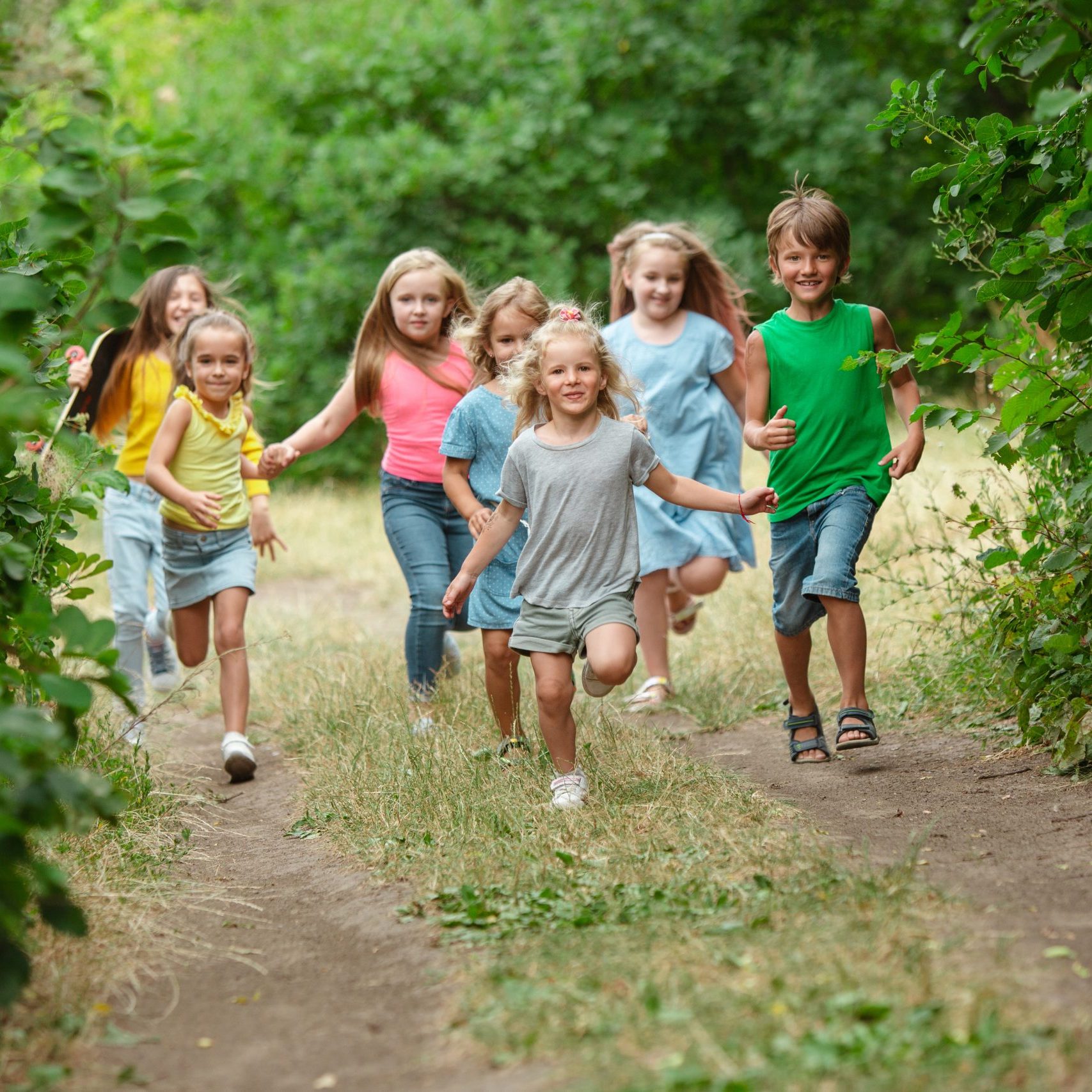 Kids, children running on green forest. Cheerful and happy boys and girs playing, laughting, running through green blooming meadow. Childhood and summertime, sincere emotions concept.
